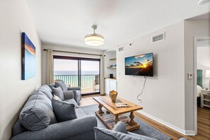 Ein modernes Wohnzimmer mit einer Couch, einem Couchtisch, einem Fernseher und einem Balkon mit Blick.