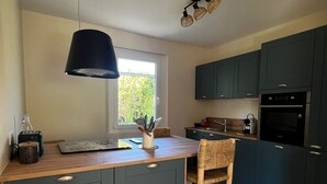 Et moderne køkken med mørke skabe, en træbordplade, en hængende lampe og et vindue, der lukker naturligt lys ind.