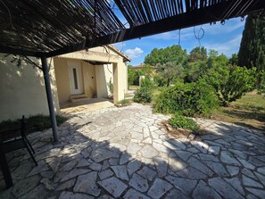 A stone-paved patio with a pergola structure, a door, and a small garden area with shrubs and trees. - Provencal house with private pool (Salernes)