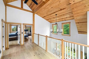 Ein geräumiges Schlafzimmer im Loft-Stil mit hohen Decken, Holzbalken und einem Balkon mit weißer Brüstung.