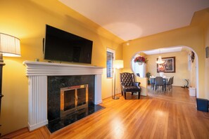 A living room with a fireplace, a television mounted above it, and a dining area with a table and chairs. - Modern Private Garden Suite Near UBC & Pacific Spirit Park
Free Parking (Vancouver)