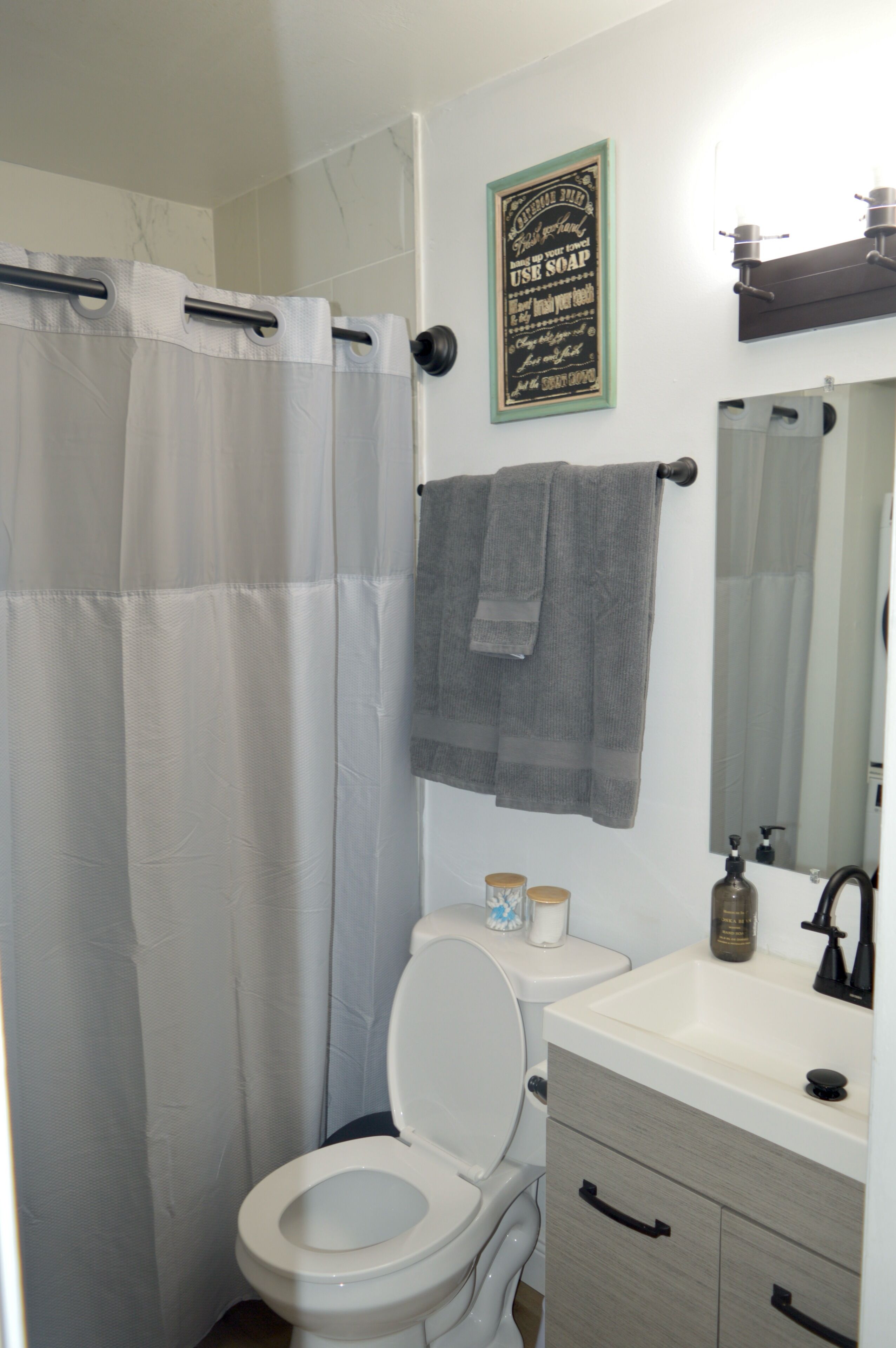 Une salle de bain comprenant des toilettes, un lavabo, un miroir, un porte-serviettes et un rideau de douche.