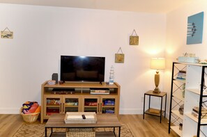 En stue med et fladskærms-tv, en træunderholdningsenhed, en lampe og en reol.