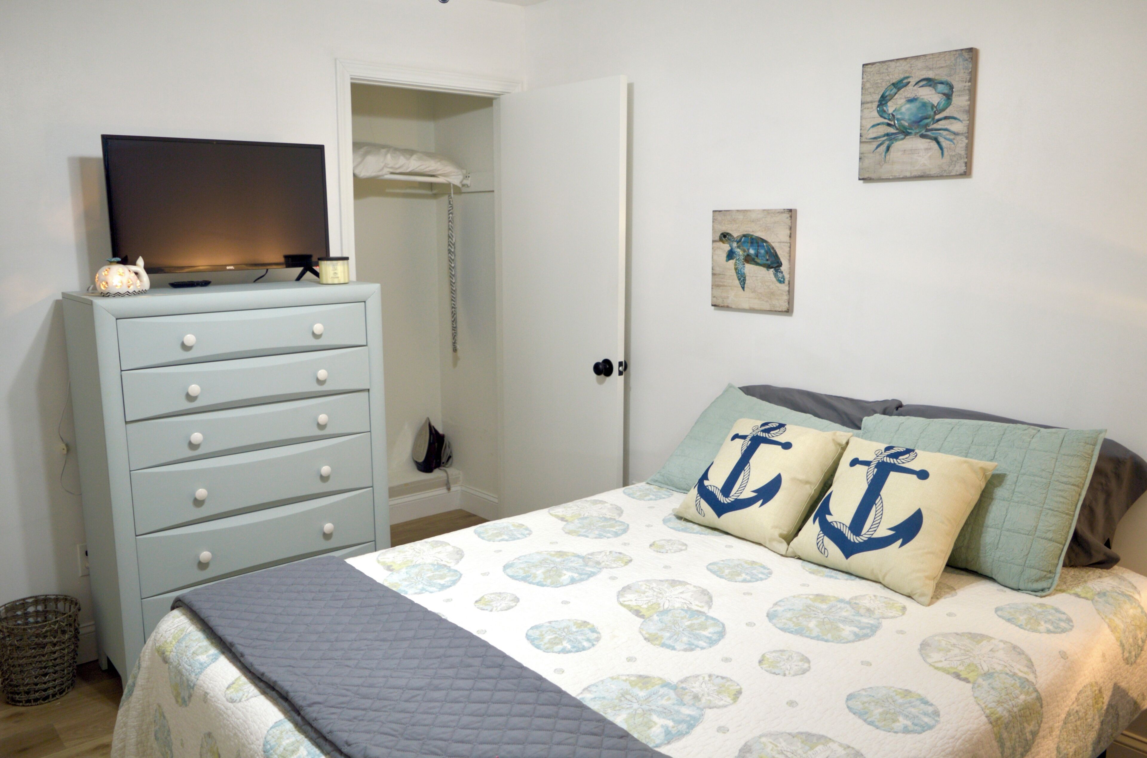 Une chambre à coucher avec un lit, une commode, un téléviseur et des œuvres d’art accrochées au mur.