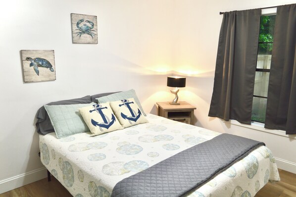 A bedroom with a bed, two pillows with anchor designs, a nightstand with a lamp, and wall art of a turtle and a crab.