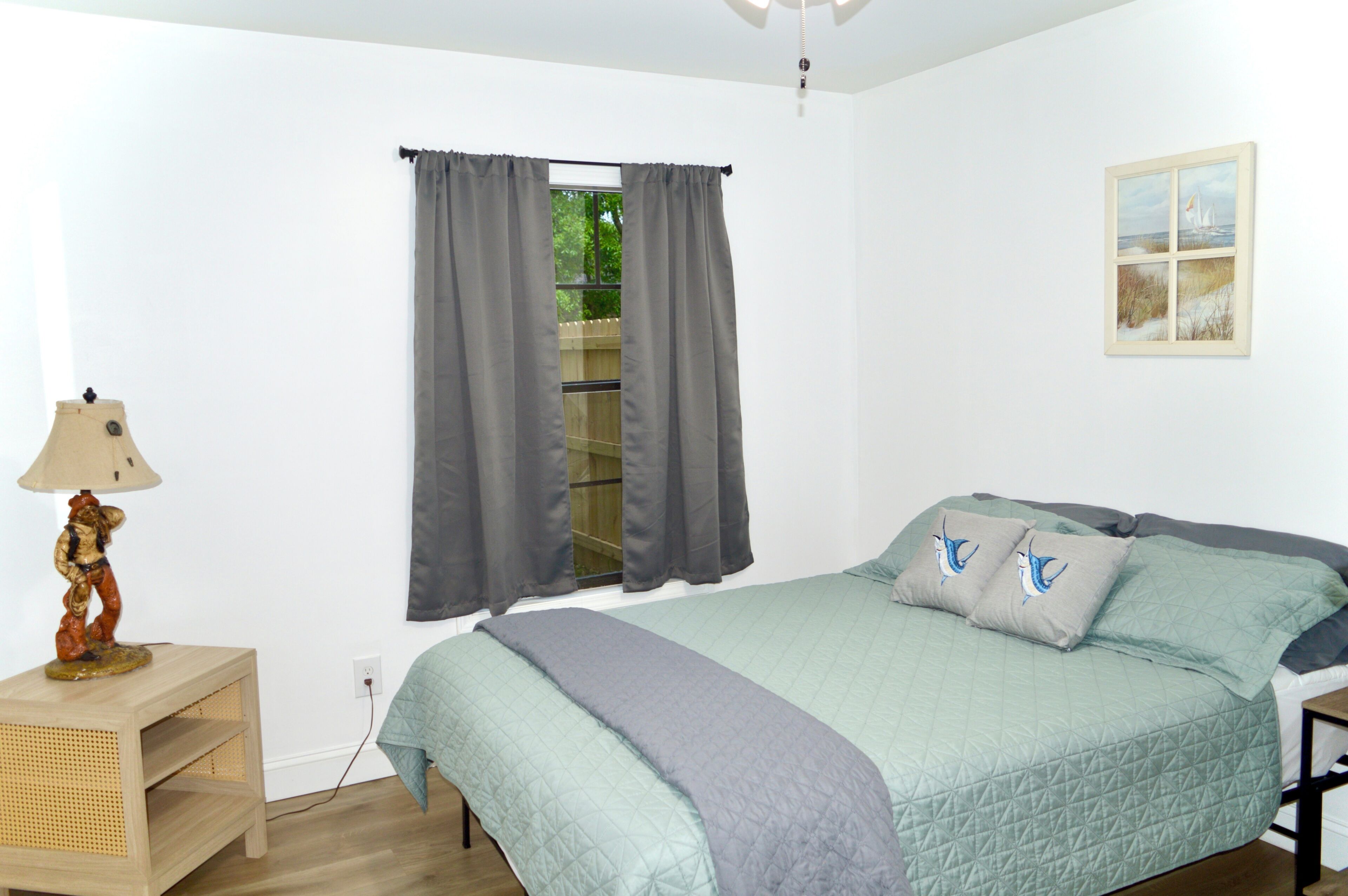 A bedroom with a bed, curtains, a lamp, a painting, and a window.