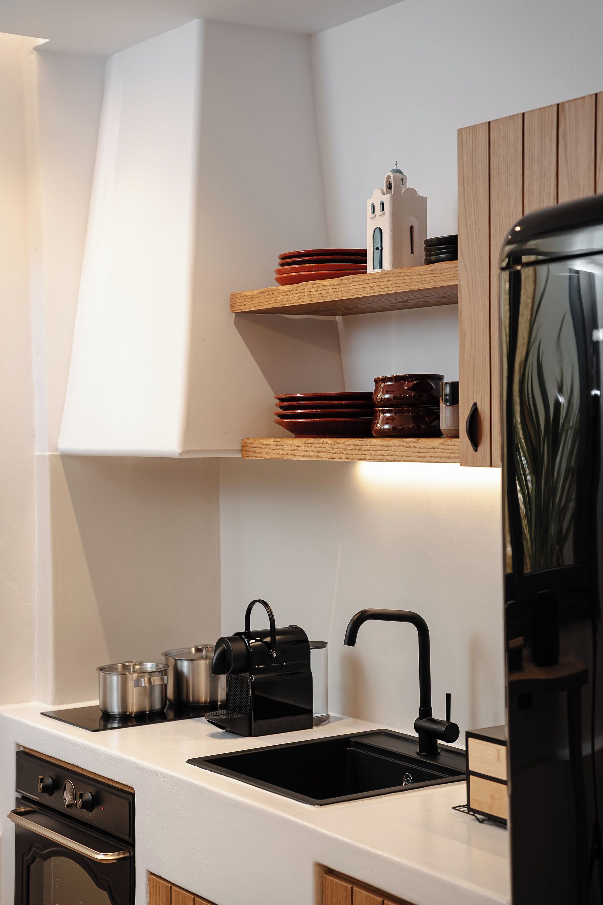 Una cocina moderna con encimera blanca, pileta negra y estantes de madera.