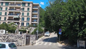 Un edificio de varios pisos con balcones, un muro de piedra y un coche estacionado en la parte delantera.