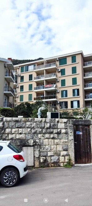 Ein mehrstöckiges Wohnhaus mit Balkonen, einer Steinmauer und einem weißen Auto.