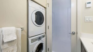 A laundry room with a front-loading washer and dryer, a towel rack with a white towel, and a door with a digital thermostat. - Serene and Calming Downtown Suite (Victoria)