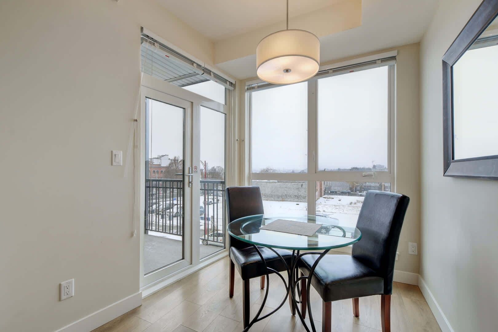 Une pièce avec une table et des chaises en verre, de grandes fenêtres et un luminaire au plafond.
