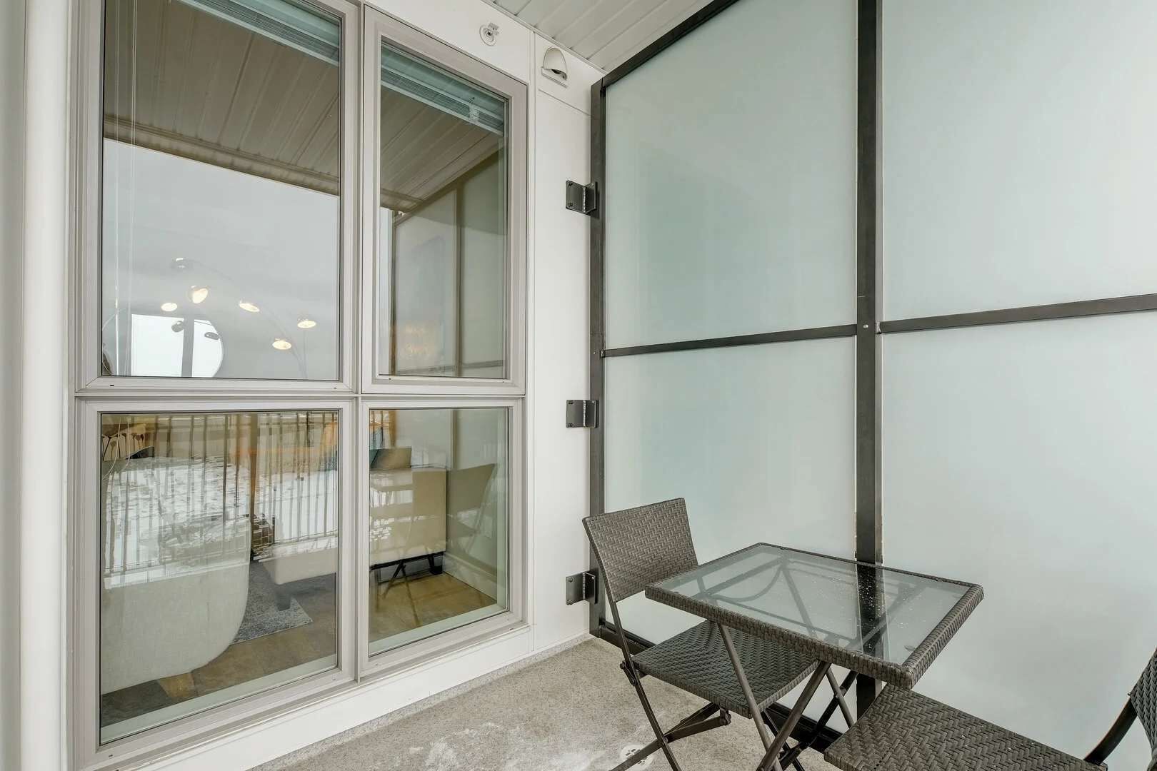 A room with a glass partition, a glass table, and two wicker chairs.
