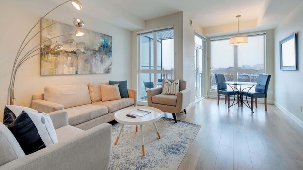 A modern living room with a sofa, armchair, coffee table, and a dining area with chairs and a table. - Serene and Calming Downtown Suite (Victoria)