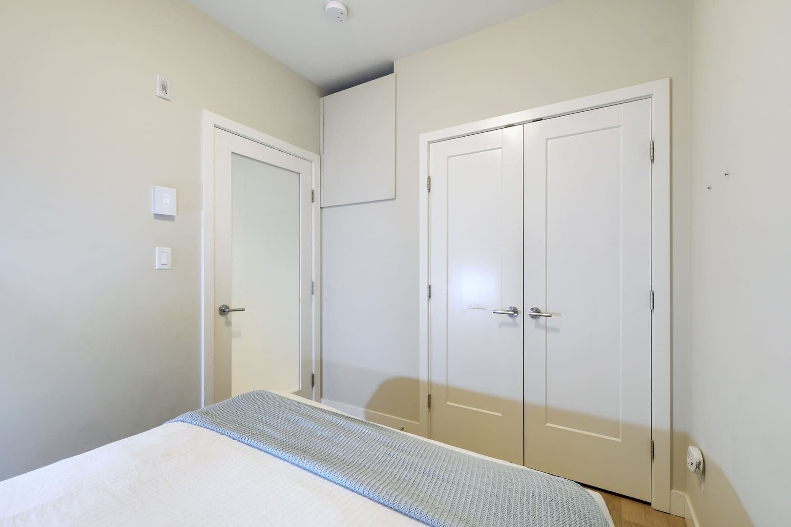 A bedroom with a bed, two white doors, and a ceiling light.