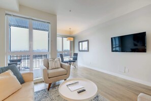 Ein modernes Wohnzimmer mit Sofa, Sessel, Couchtisch und einem an der Wand befestigten Fernseher.