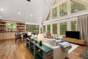 A spacious living area with a kitchen, large windows, and a television. - Black Bear Cabin.  Luxury 2bed/2 bath, 13 miles to Eureka Springs on Table Rock. (Eagle Rock)