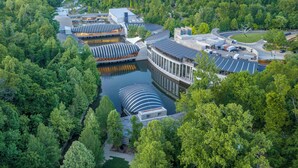 Luchtbeeld van een modern gebouwcomplex met een centraal waterpartij, omgeven door weelderige begroeiing.