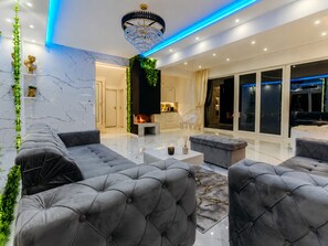 Ein modernes Wohnzimmer mit Kamin, grauen Polster-Sofa und Couchtisch, sowie einer Kandelaber-Leuchte.