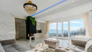 A modern living room with a fireplace, large windows, and a view of mountains.