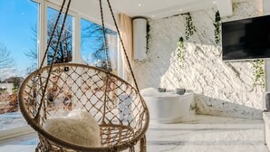 A modern room with a hanging chair, a bathtub, and a large TV.
