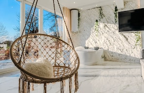 A modern room with a hanging chair, a bathtub, and a large TV.