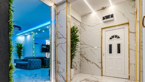A modern lobby with a marble floor, a blue-lit ceiling, a seating area with a blue sofa, and a white door with gold trim.