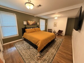 Ein Schlafzimmer mit einem großen Bett, zwei Nachttischlampen, einem Deckenventilator, einem Teppich und einem an der Wand befestigten Fernseher.