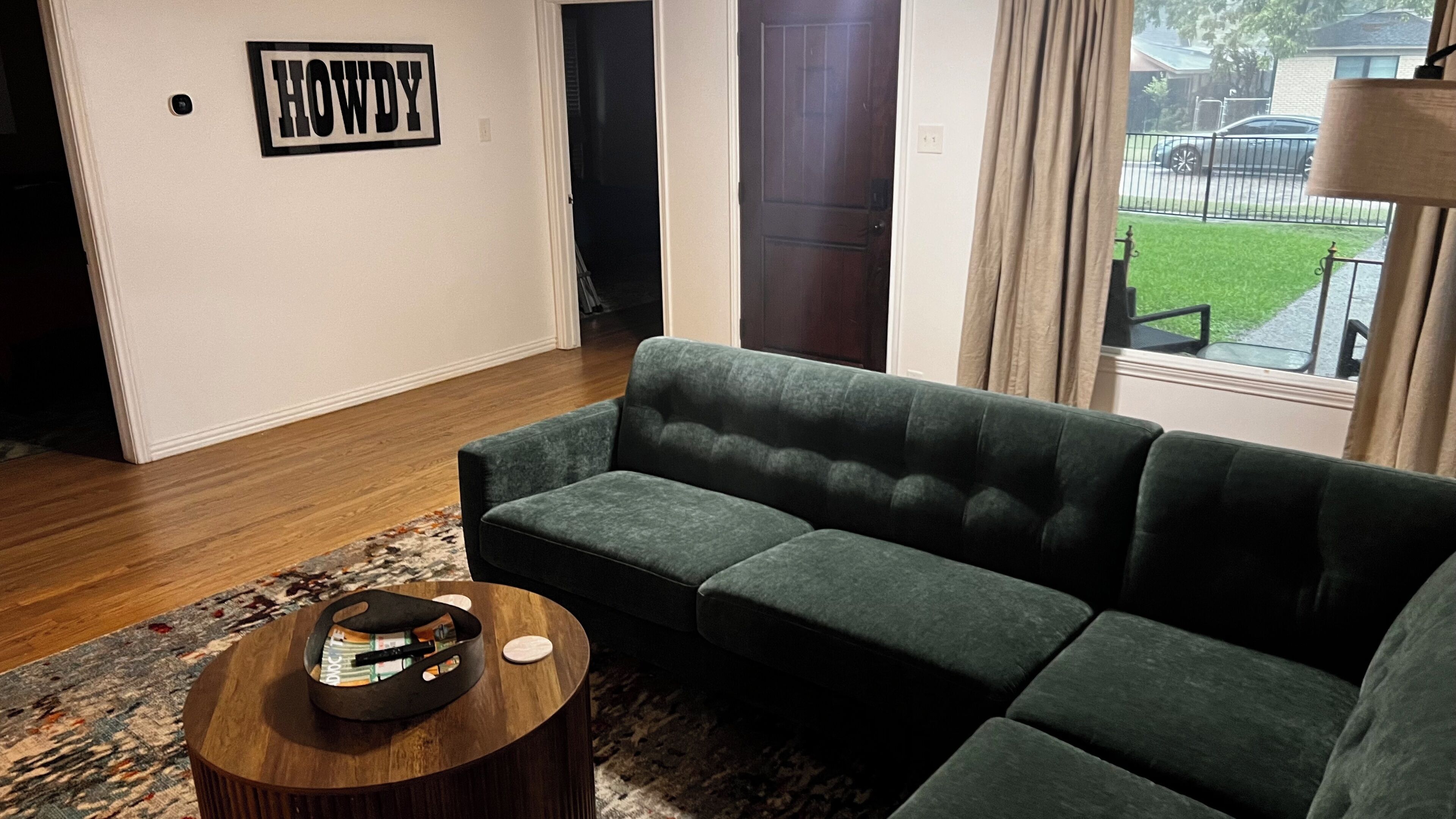 Una sala de estar con un sofá verde, una mesa de centro redonda de madera y un cartel con la palabra 'HOWDY' en la pared.