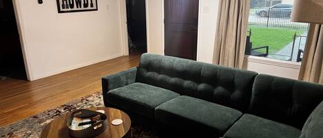 Una sala de estar con un sofá verde, una mesa de centro redonda de madera y un cartel con la palabra 'HOWDY' en la pared.