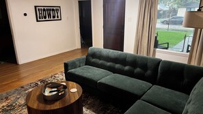Ein Wohnzimmer mit einem grünen Sofa, einem runden Couchtisch und einem 'HOWDY'-Schild an der Wand.