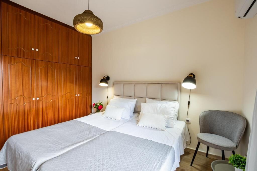 A bedroom with a bed, bedside lamps, a chair, and a wooden wardrobe.