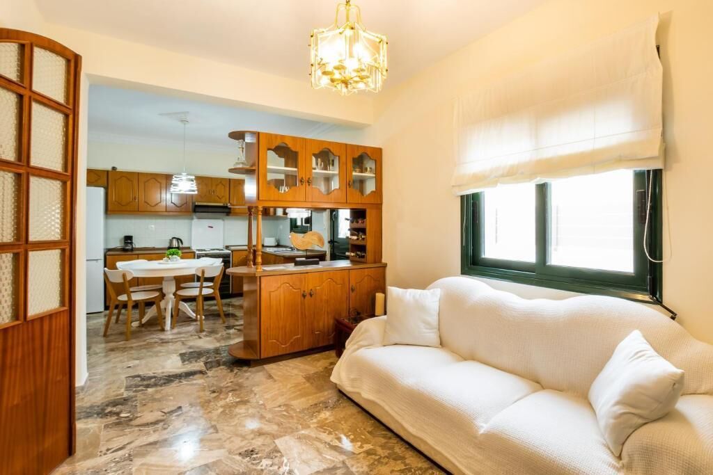 A living room with a sofa, a dining table with chairs, a kitchen area with cabinets, and a chandelier.