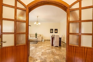 A room with a wooden door, a marble floor, a sofa, a dining table, and a chandelier. - Villa Maria (Karpathos)