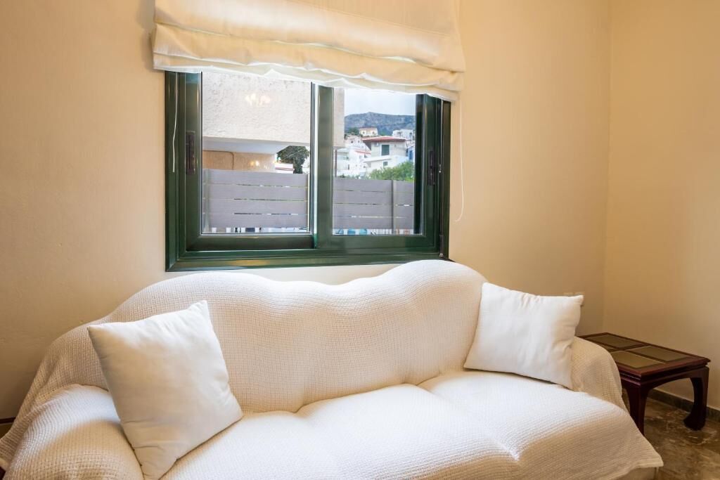 Um sofá branco com vista para edifícios através de uma janela e uma mesa de madeira.