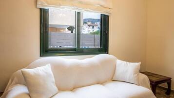 Um sofá branco com vista para edifícios através de uma janela e uma mesa de madeira.