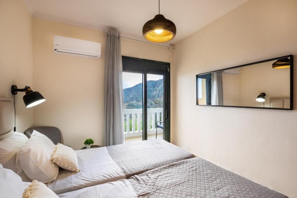 Habitación de hotel con cama, escritorio, silla, lámpara, espejo y balcón con vista a la montaña.