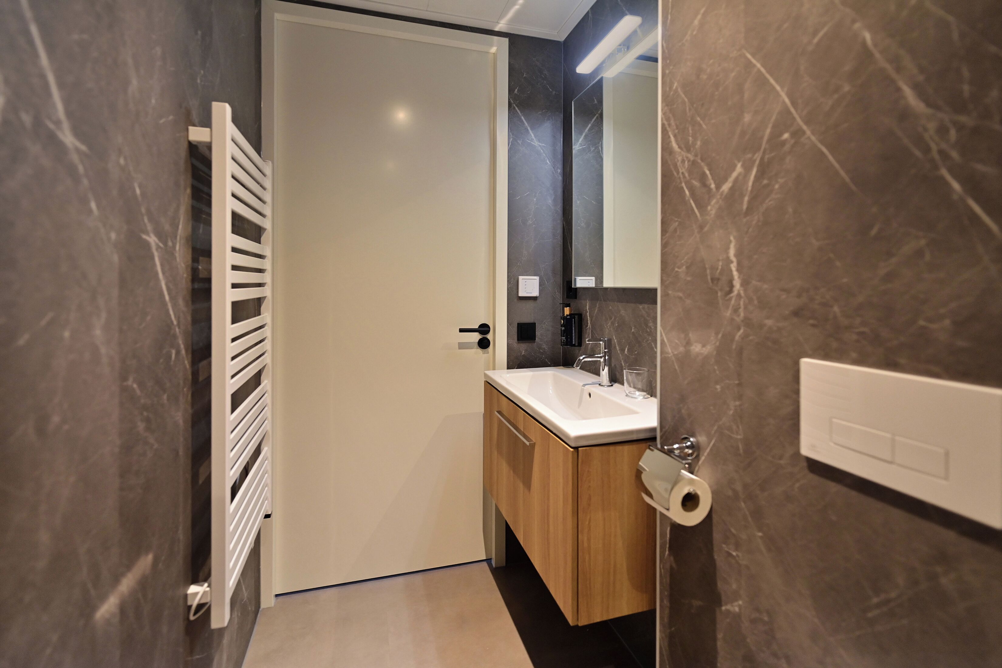 Un baño moderno con una puerta blanca, un tocador de madera, un espejo y un dispensador de papel higiénico.