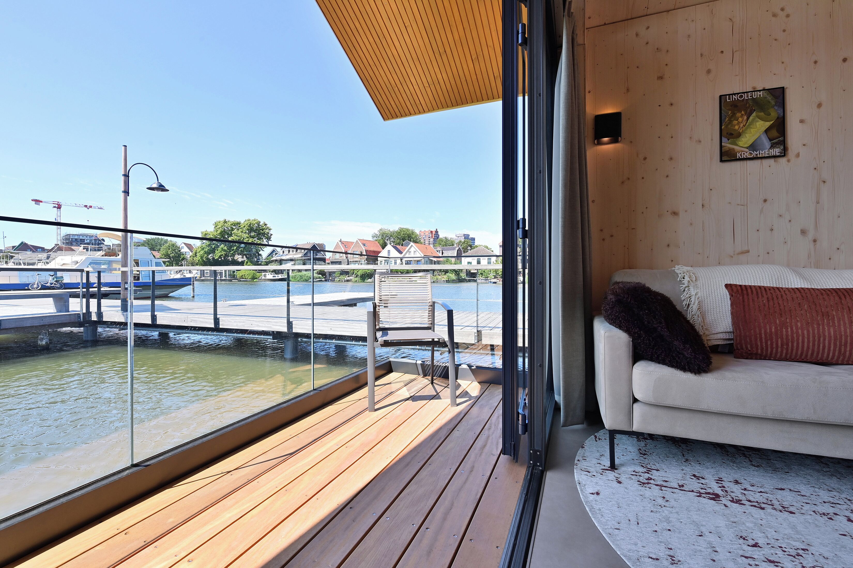 A modern interior with a wooden deck overlooking a marina, a sofa with cushions, and a framed picture on the wall.