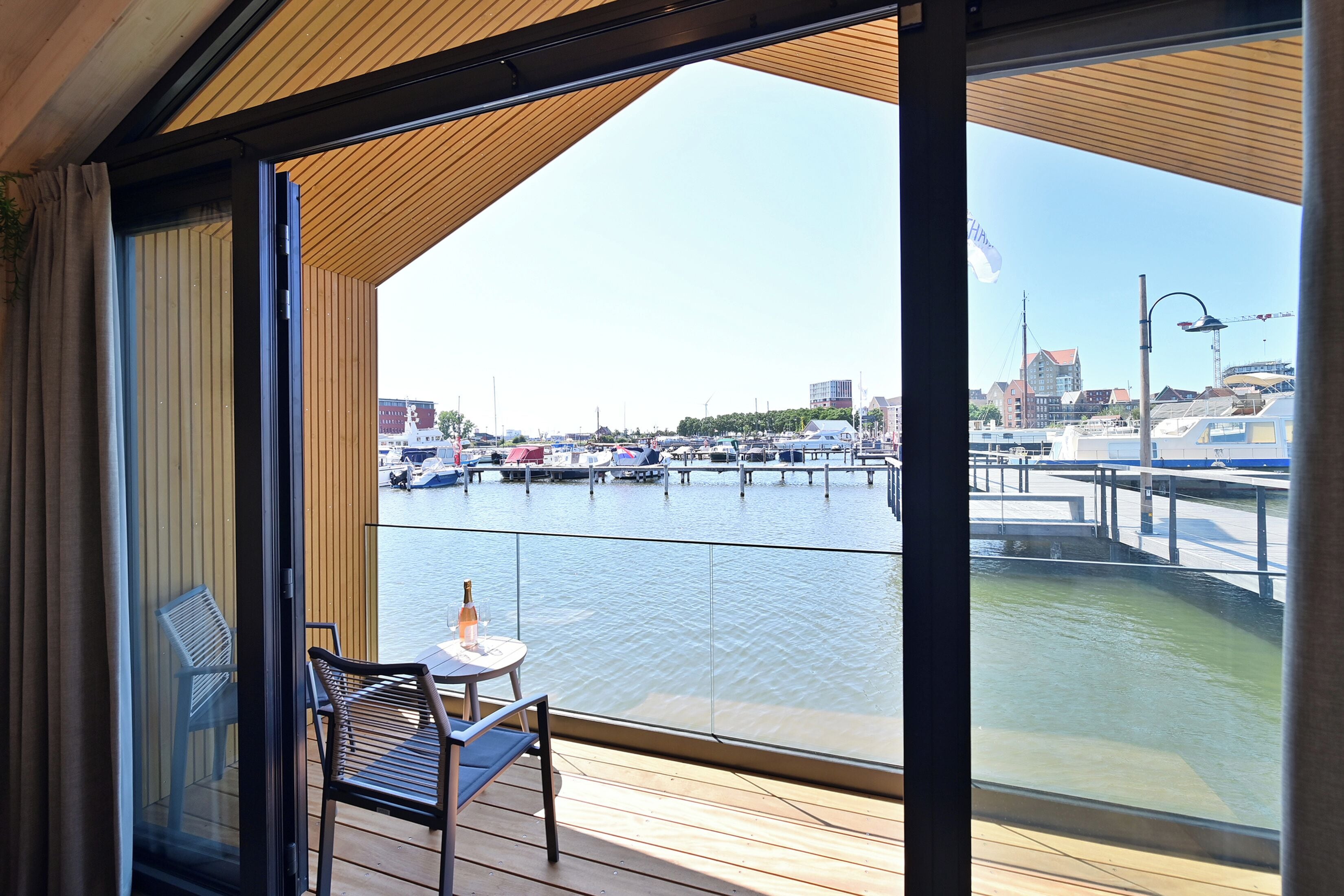A balcony with a view of a marina, a table with a bottle, and a chair.