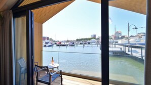 A balcony with a view of a marina, a table with a bottle, and a chair.