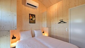 A bedroom with a wooden wall, a bed with white bedding, an air conditioning unit, a poster, a coat hanger, and a thermostat.