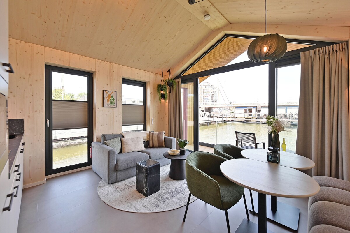 A modern interior with a sofa, chairs, a table, and a view of a water body outside.