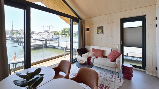 A modern living room with a view of a water body and dock, a white sofa, a coffee table, and a dining area with chairs.