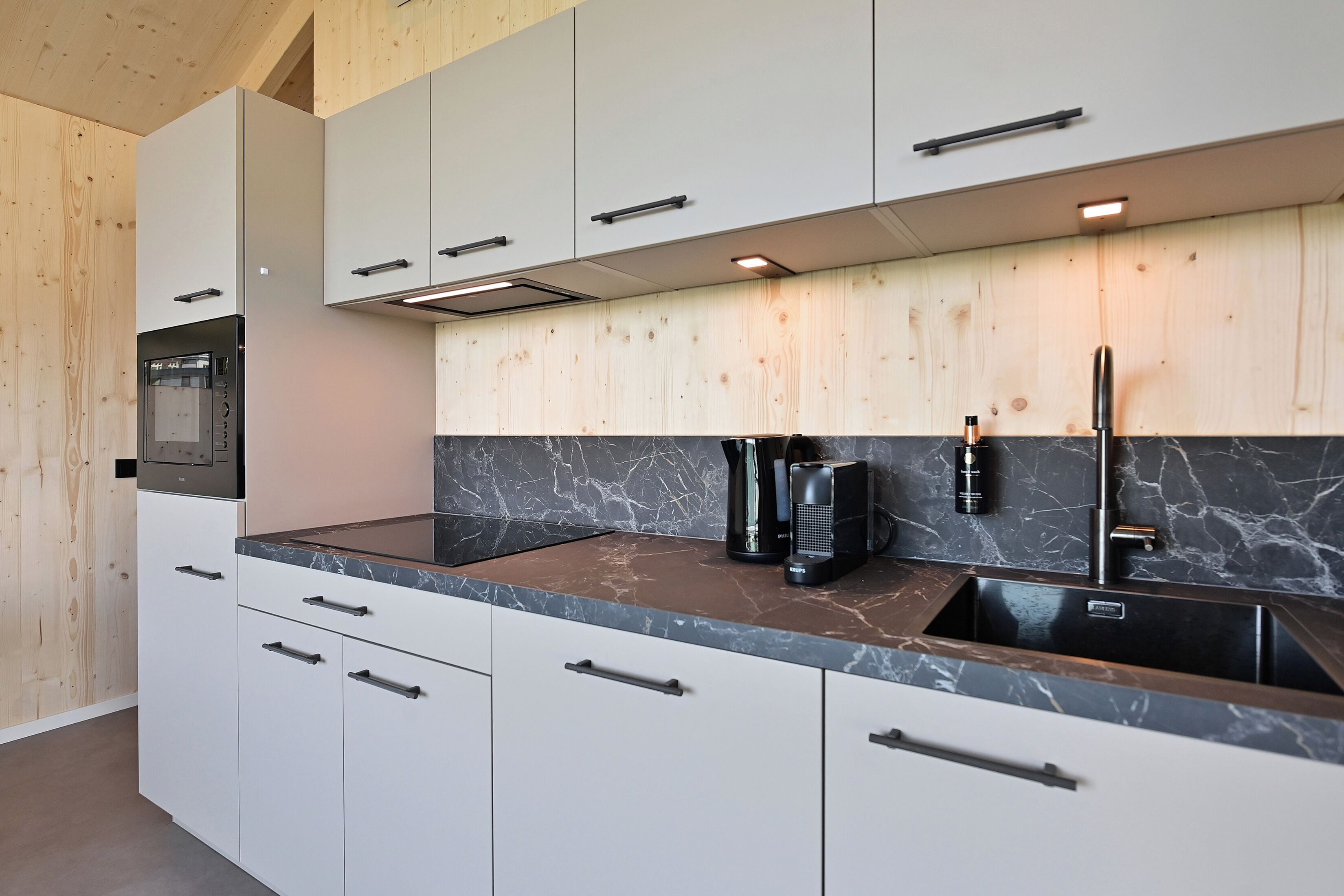 Una cocina moderna con armarios blancos, encimera de mármol y horno empotrado.