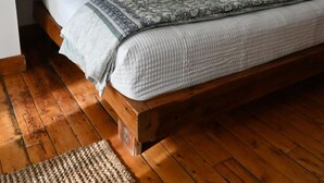 Ein Einzelbett mit Holzrahmen, weißer Bettwäsche und einer gemusterten Tagesdecke. Ein Holzboden und ein kleiner Teppich liegen vor dem Bett.