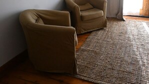 Ein Zimmer mit einem an der Wand montierten Flachbildfernseher, zwei braunen Sesseln, einem gewebten Teppich und einem Holzboden.