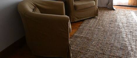 A room with a flat-screen TV mounted on the wall, two brown armchairs, a woven rug, and a wooden floor.