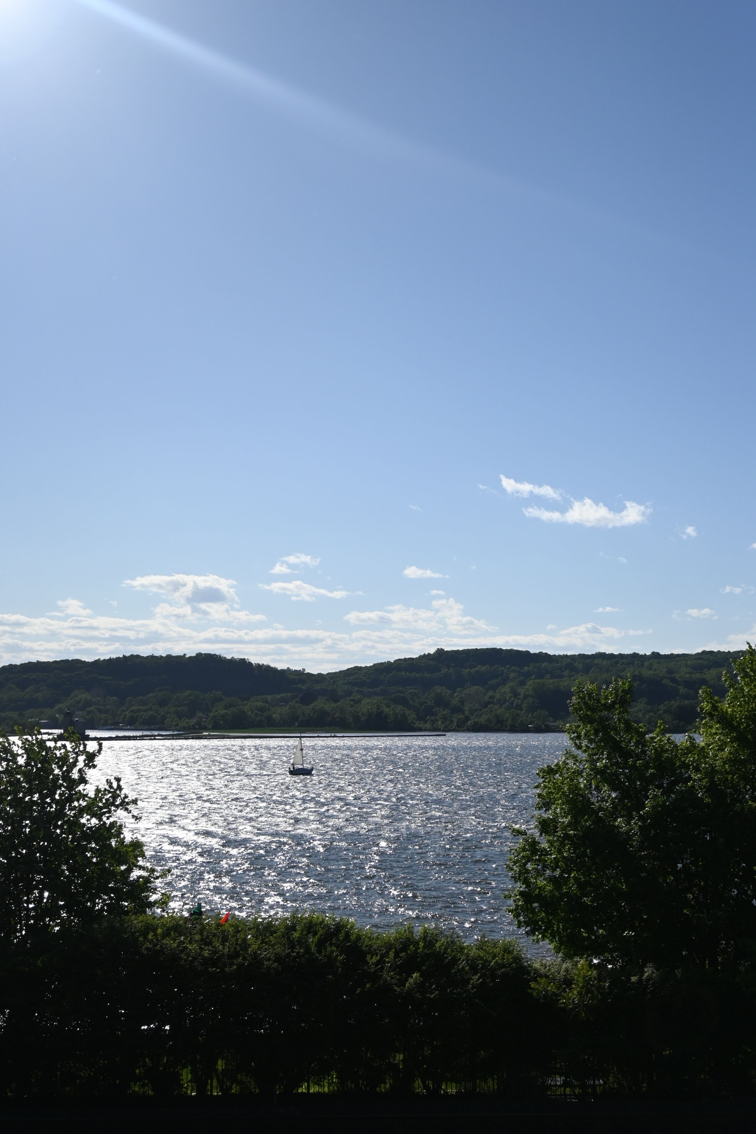 A lake with a sailboat, surrounded by trees and hills.