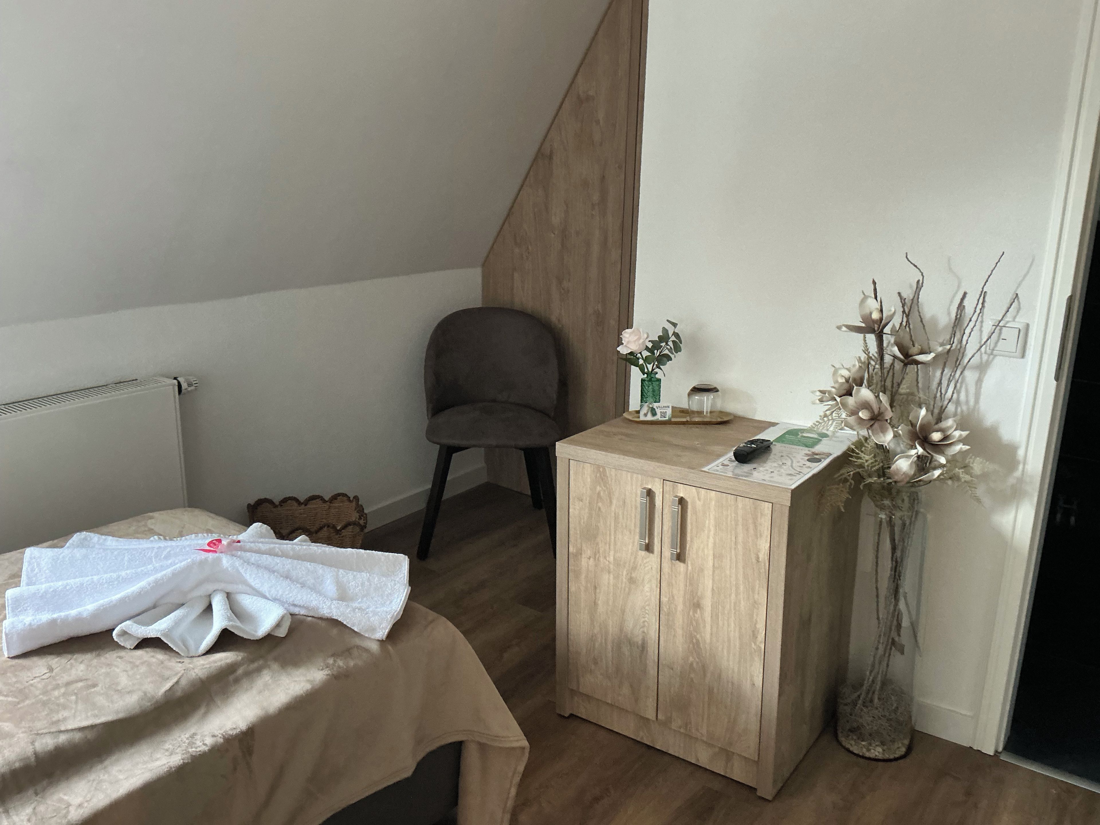 A bedroom with a bed, a wooden cabinet, a chair, and a vase with flowers.