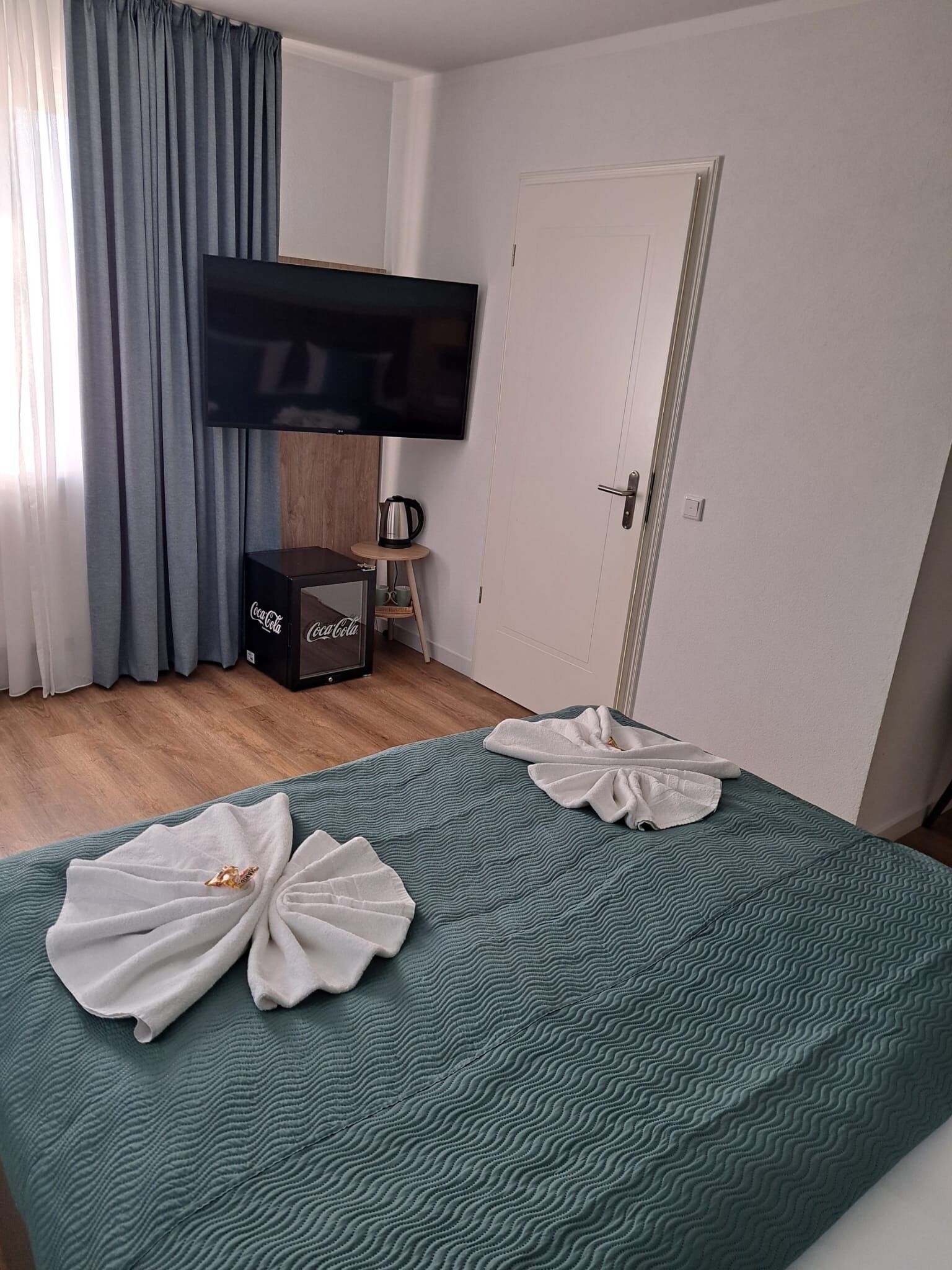 Quarto de hotel com uma cama, televisão de tela plana na parede, cafeteira e uma porta.